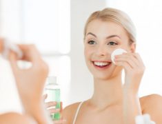 A Smiling Woman Appliying Cream On Her Face Infront Of The Mirror.
