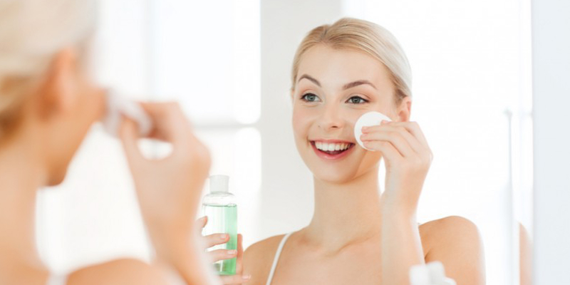 A Smiling Woman Appliying Cream On Her Face Infront Of The Mirror.