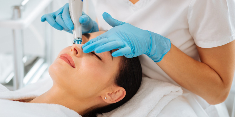 A Beautician Applies Facial Cream On A Young Woman Face.