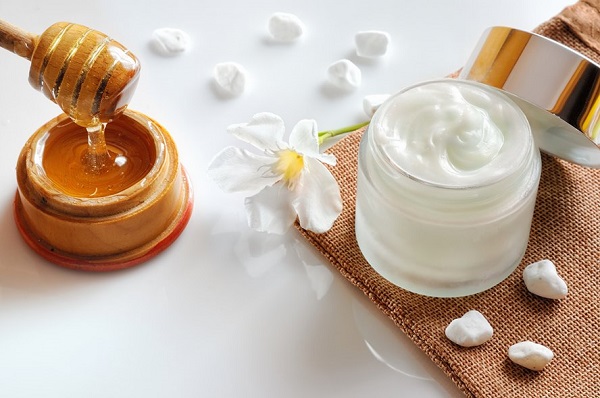 A Table Which Consists Of A Facial Cream & A Wooden Bowl Of Honey.