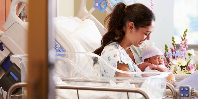 A Smiling Mother With Her Kiddo After Delivery In Hospital.