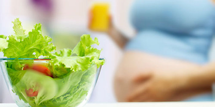 A Bowl Having Green Veggies In A Blur Background of Pregnant Woman.