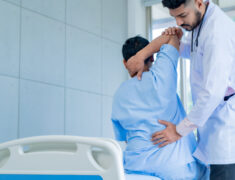 A physiotherapist explains stretching exercises to a patient with back pain during treatment in a hospital.